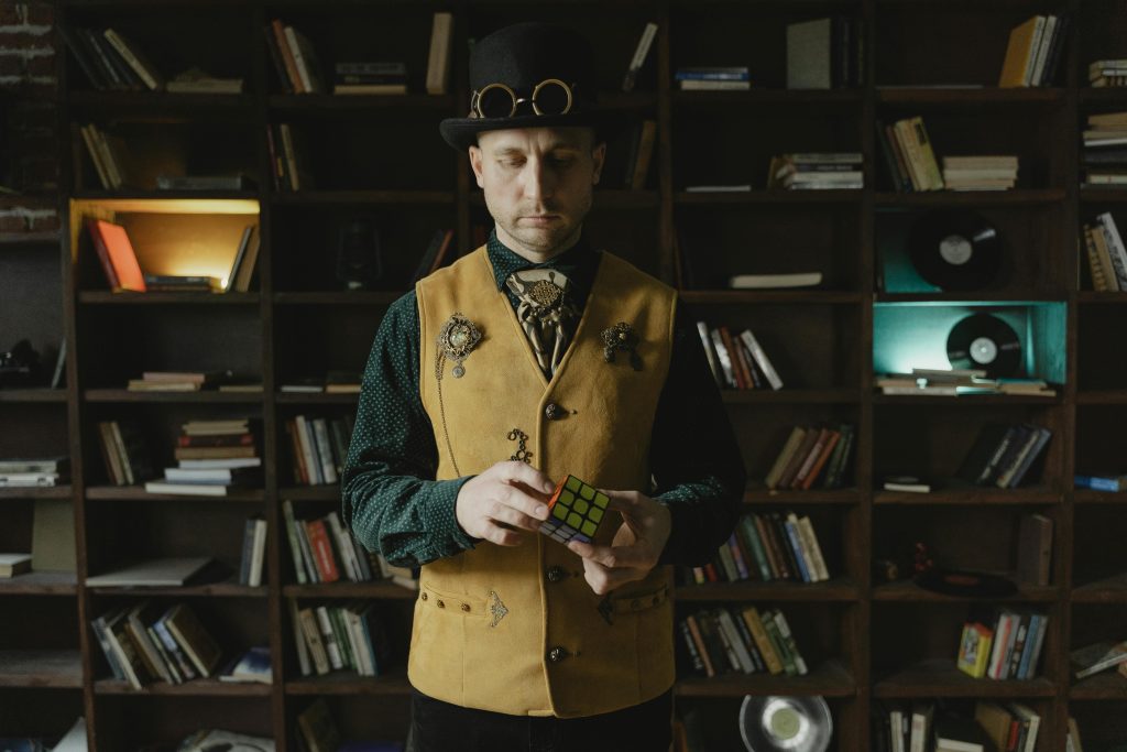 A steampunk-styled man with a Rubik's Cube stands in a vintage library setting.